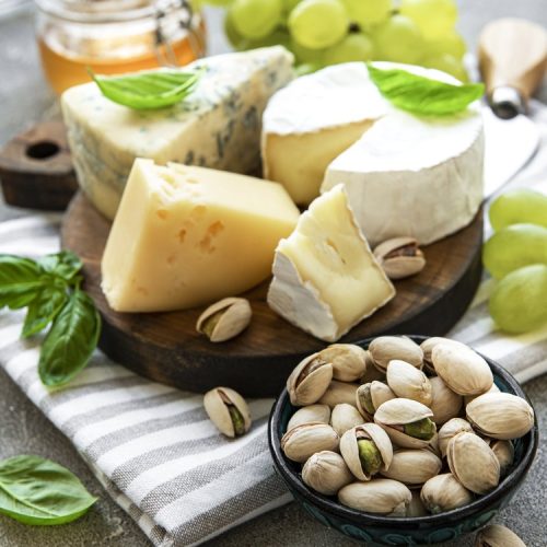 Various types of cheese, grapes and snacks on a grey concrete background